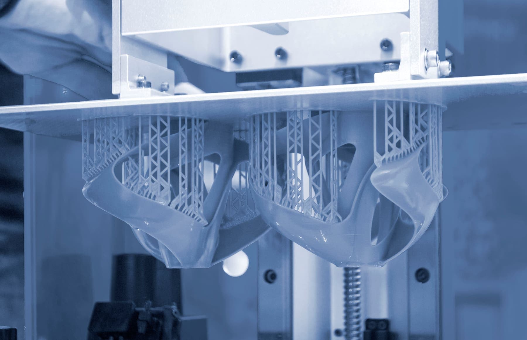 Resin 3D printed parts hanging upside down from a resin printer's build plate on thin support structures